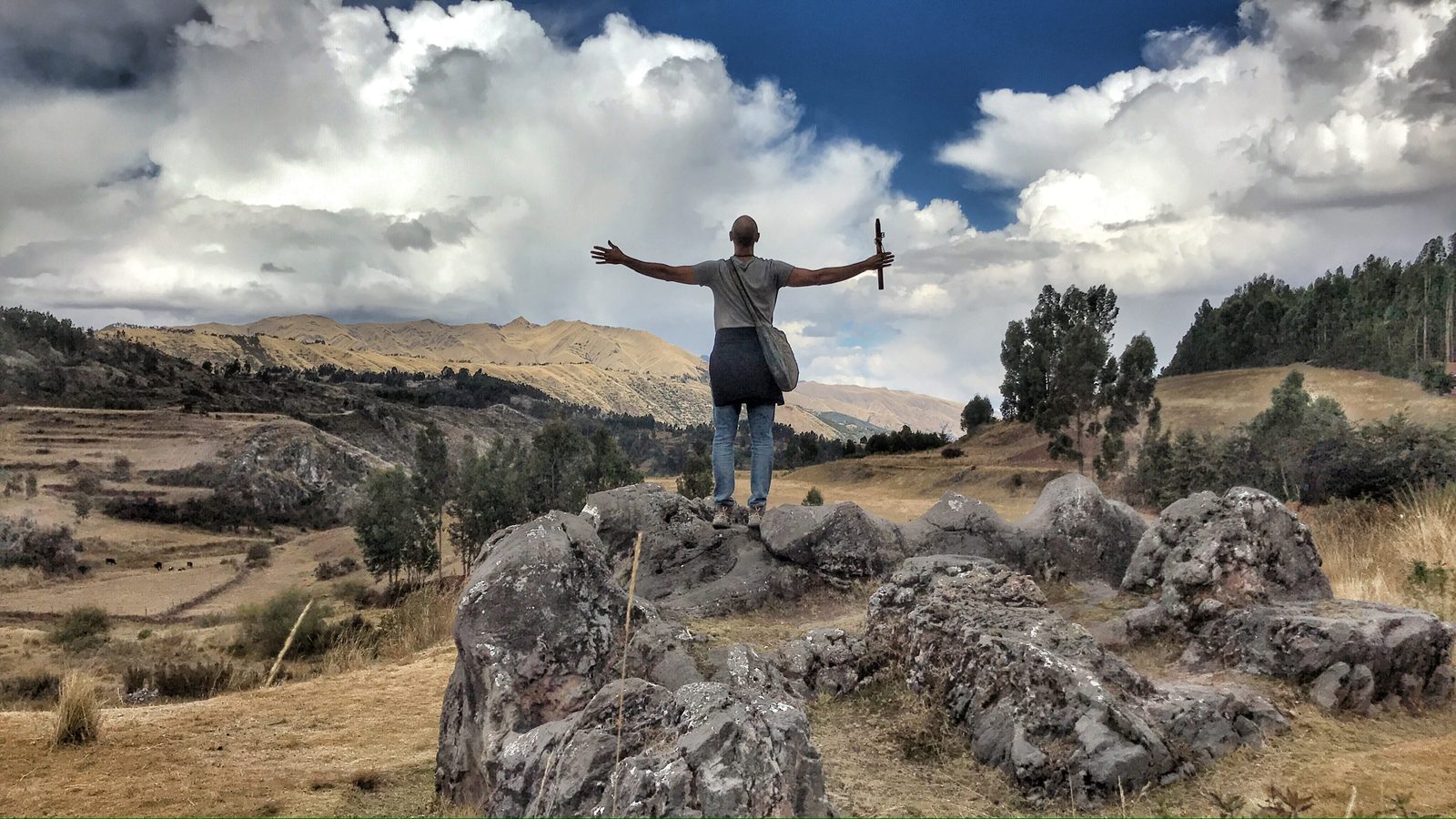 Someone standing on a rock outcrop with both arms raised toward the sky