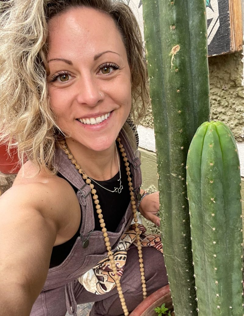 Dani Reardon beside a tall Huachuma column, smiling at the camera