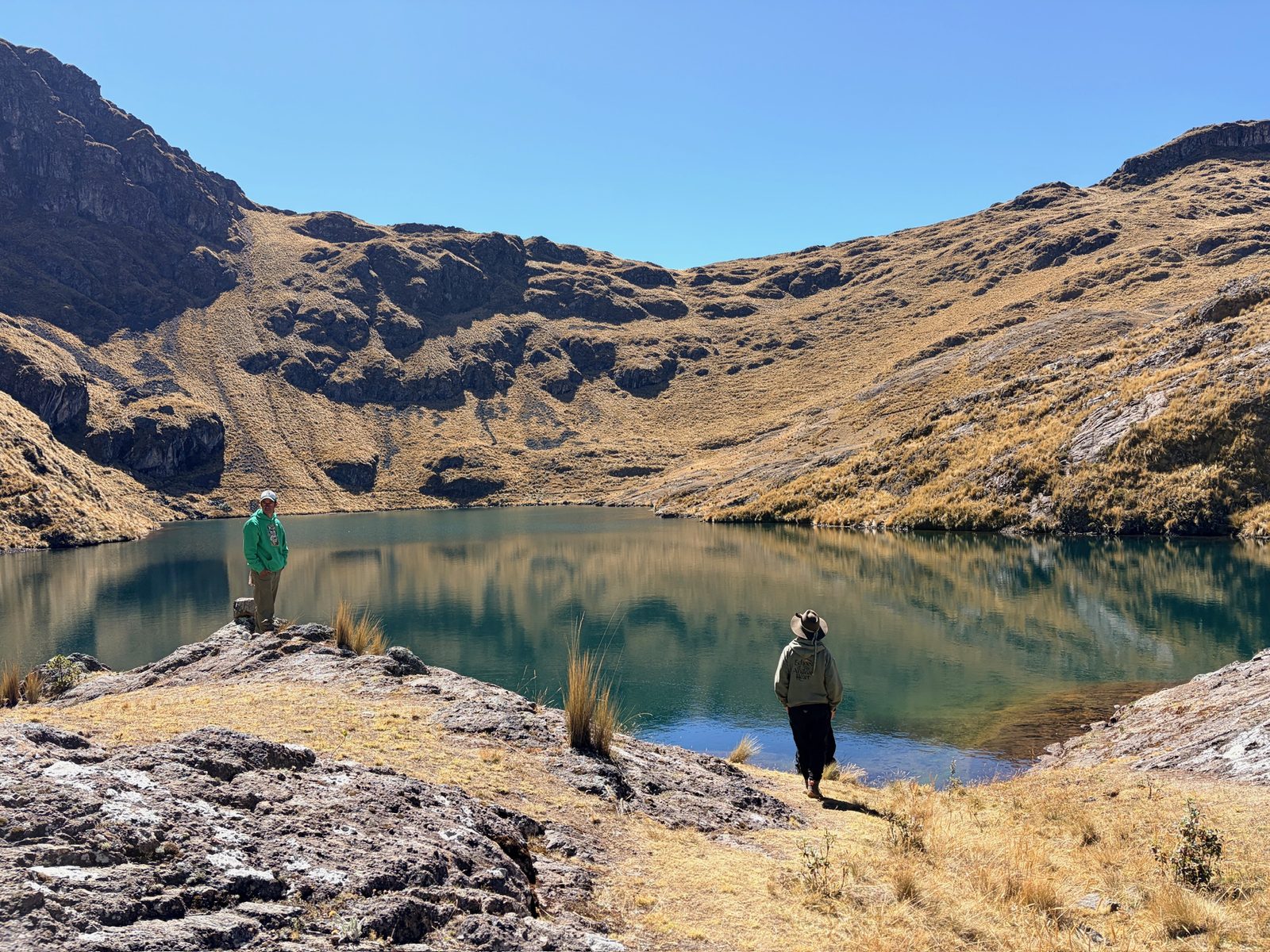 A still lake below a bare mountain ridge, with two people standing on the shore