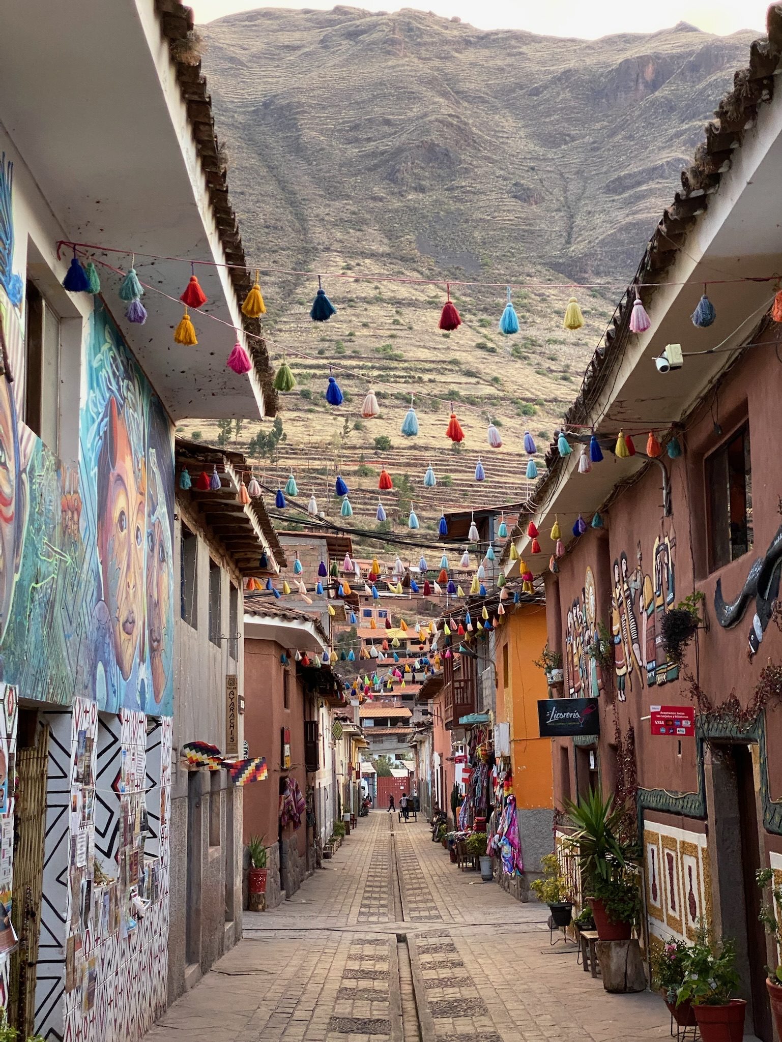 A narrow street in Pisac hung with bunting, its painted walls running toward the mountains