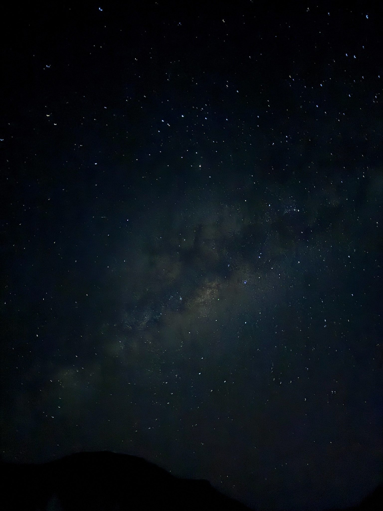 A night sky crowded with stars and the faint band of the Milky Way above the dark line of a ridge