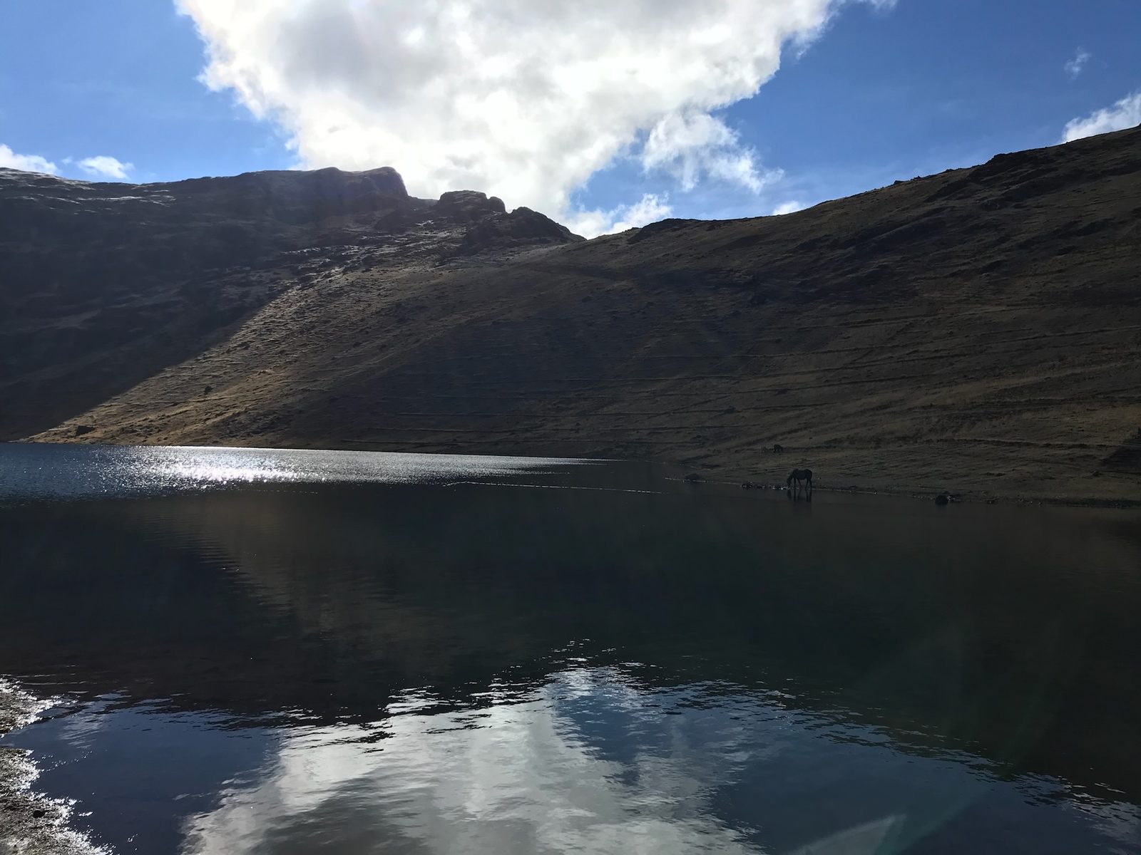 A still lake holding the reflection of a dark mountain and a bank of cloud