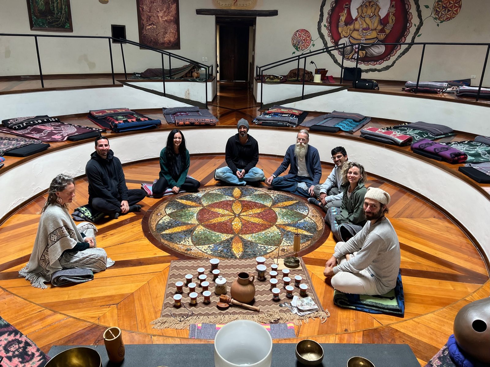People sitting in a circle on the floor around a painted mandala set with singing bowls