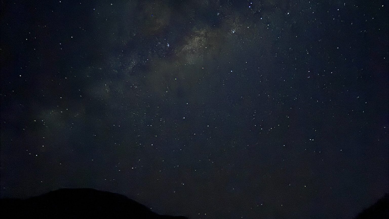 The Milky Way across a dark sky full of stars above the black outline of the mountains