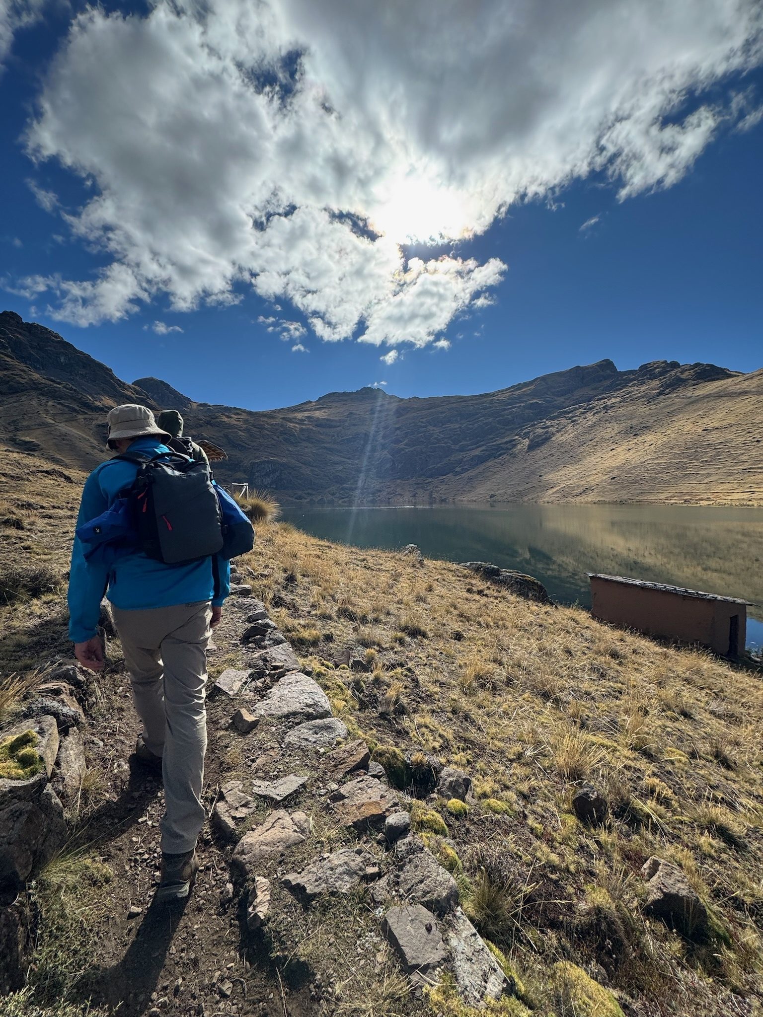 Two walkers following a stone edged path along a high lake under a bright bank of cloud