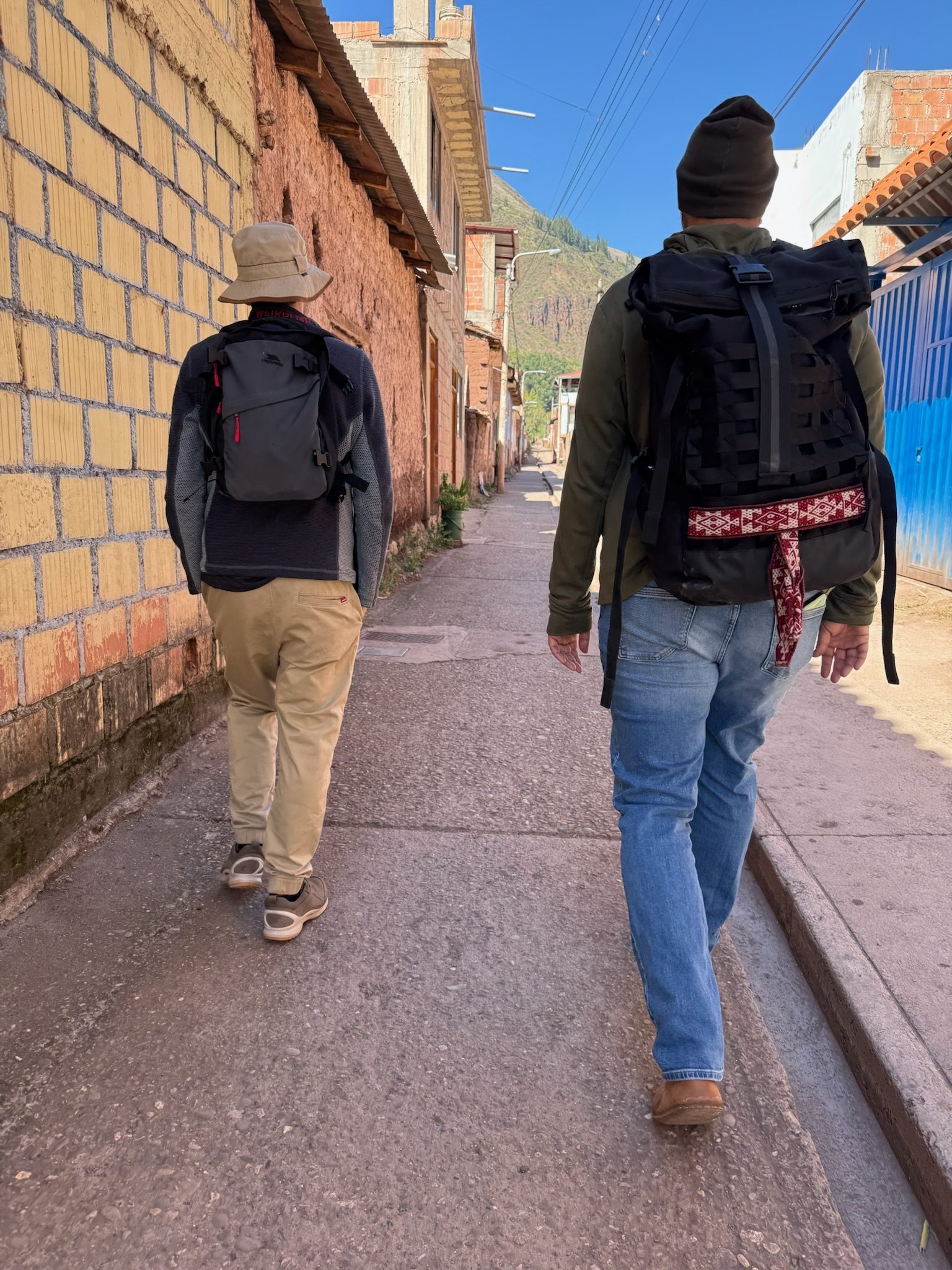 Two people with rucksacks walking away down a narrow street in Pisac between brick walls