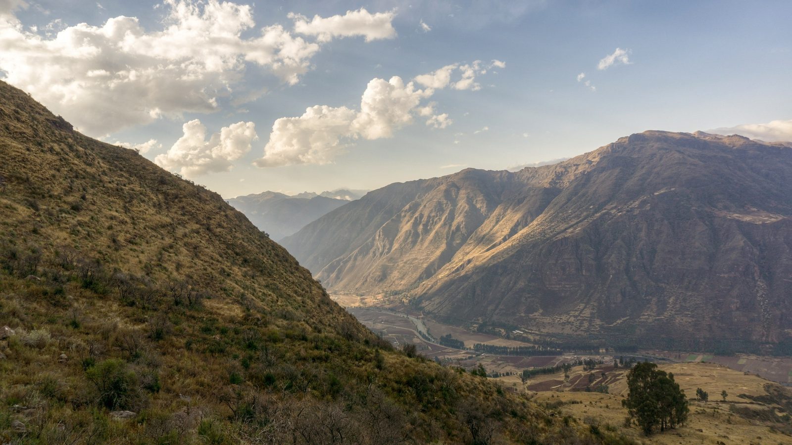 A steep valley of dry grass and rock falling toward distant mountains