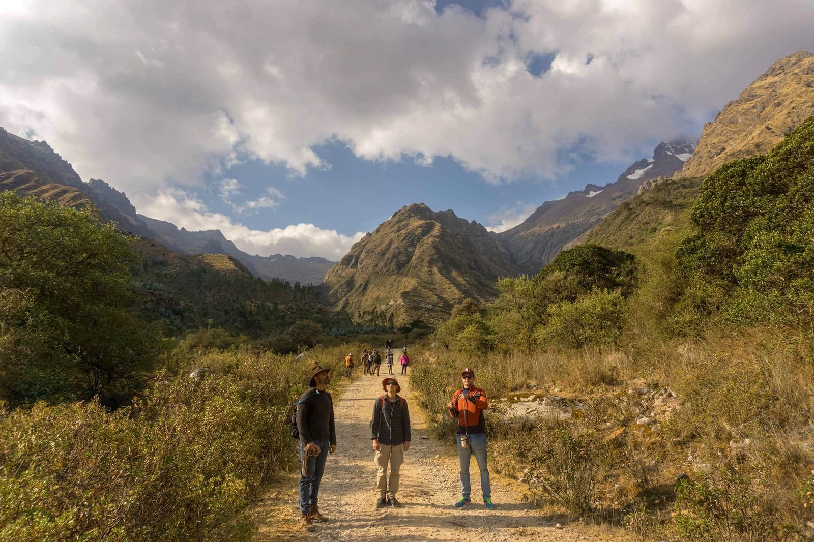 Three walkers standing on a trail with a wide valley and mountains behind them