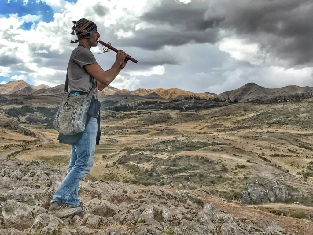 Someone standing on rock high above a valley, playing a wooden flute