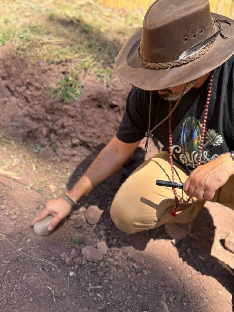 Someone in a wide brimmed hat kneeling to set a huachuma cutting into the earth at the Sanctuary