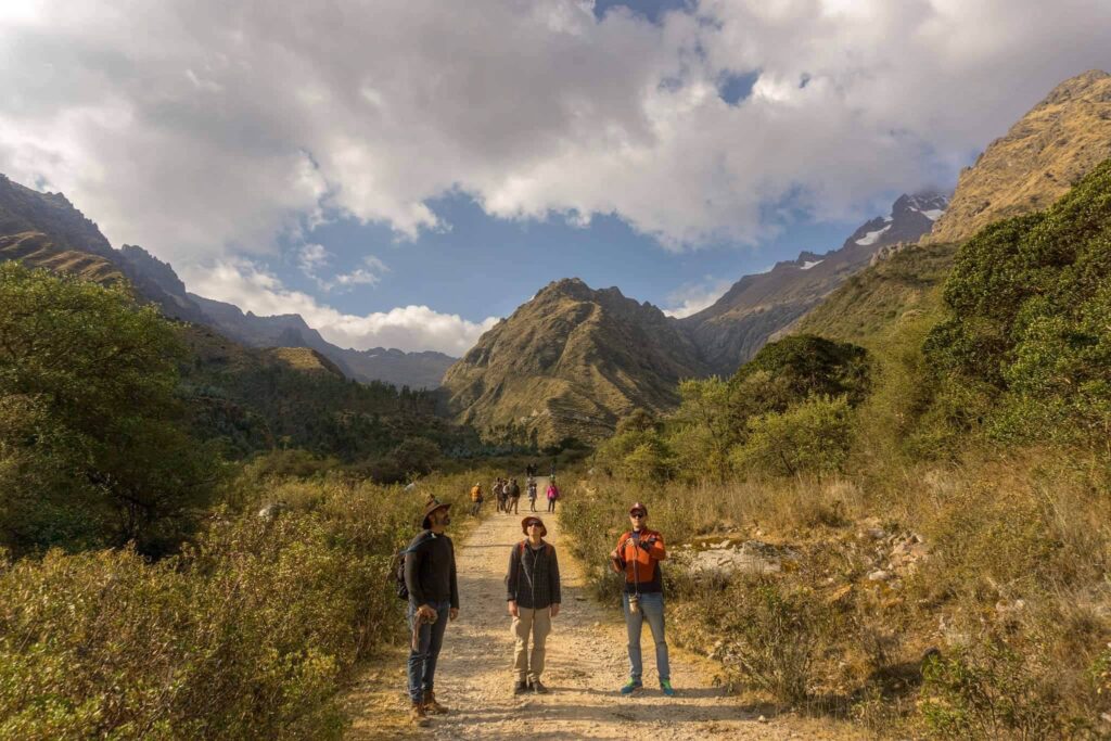 Three walkers seen from behind following a trail towards a line of mountains